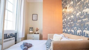Une chambre à coucher comprenant un lit, une table de chevet, une commode et un mur recouvert d’un papier peint à motifs animaliers.