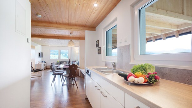A modern kitchen with wooden beams, a large window, and a dining area with a table and chairs. - Hochtalblick: Apartment "Blösling 1" with Panoramic View, Wi-Fi & DreiWelten-Card Included (Bernau im Schwarzwald)
