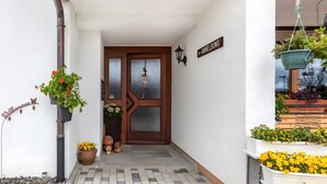 A building entrance with a brown door, a welcome sign, a potted plant, and a hanging planter. - Hochtalblick: Apartment "Blösling 1" with Panoramic View, Wi-Fi & DreiWelten-Card Included (Bernau im Schwarzwald)