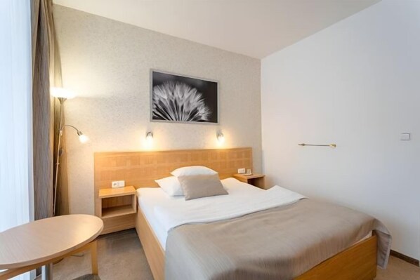 Une chambre d’hôtel avec un lit, des tables de chevet, une petite table et un tableau accroché au mur.