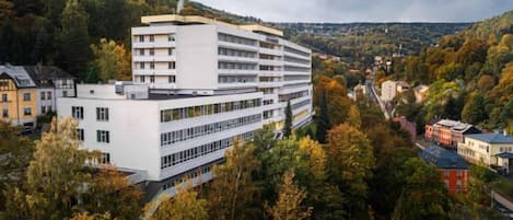 A multi-story building with a modern architectural design, surrounded by a forested area.
