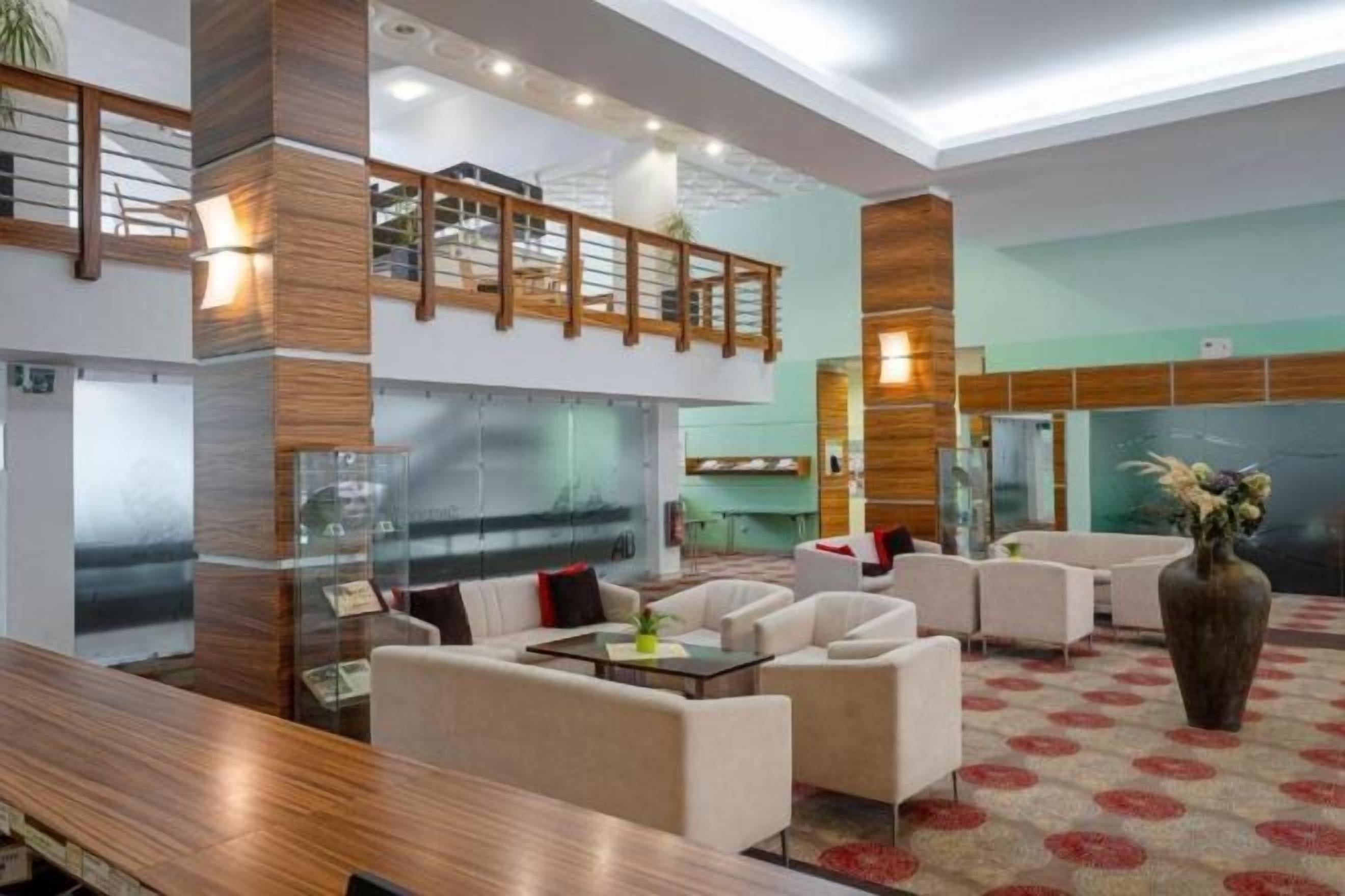 A hotel lobby with a high ceiling, a wooden staircase, and a seating area with sofas and a coffee table.