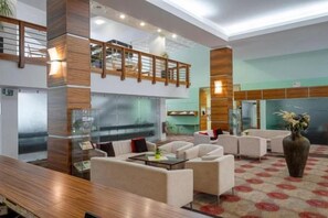 Eine Hotelhalle mit hoher Decke, einer Holztreppe und einer Sitzecke mit Sofas und einem Couchtisch.