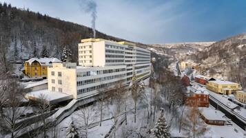 A multi-story building with a central atrium, surrounded by snow-covered trees and a mountainous backdrop.