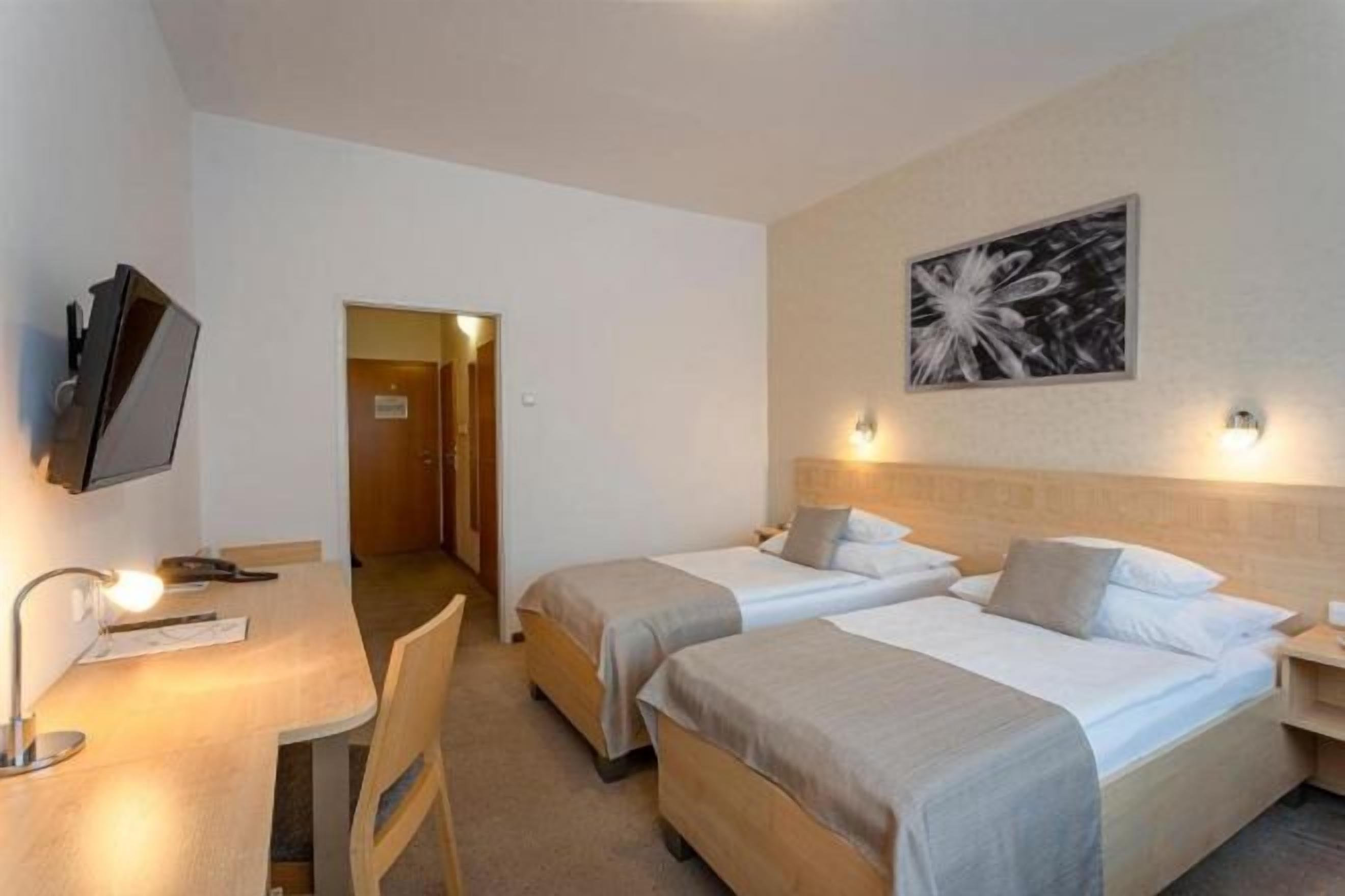 A hotel room with two beds, a desk with a chair, a TV, and a painting on the wall.