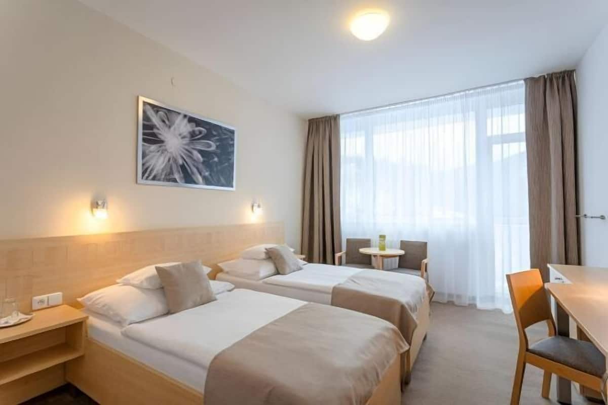 A hotel room with two beds, a small table, a chair, and a window with curtains.