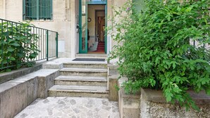 Eine Steintreppe führt zu einem Hauseingang mit einer grünen Tür, einem kleinen Fenster mit Gitterstäben und einem grünen Topf mit Pflanzen daneben.