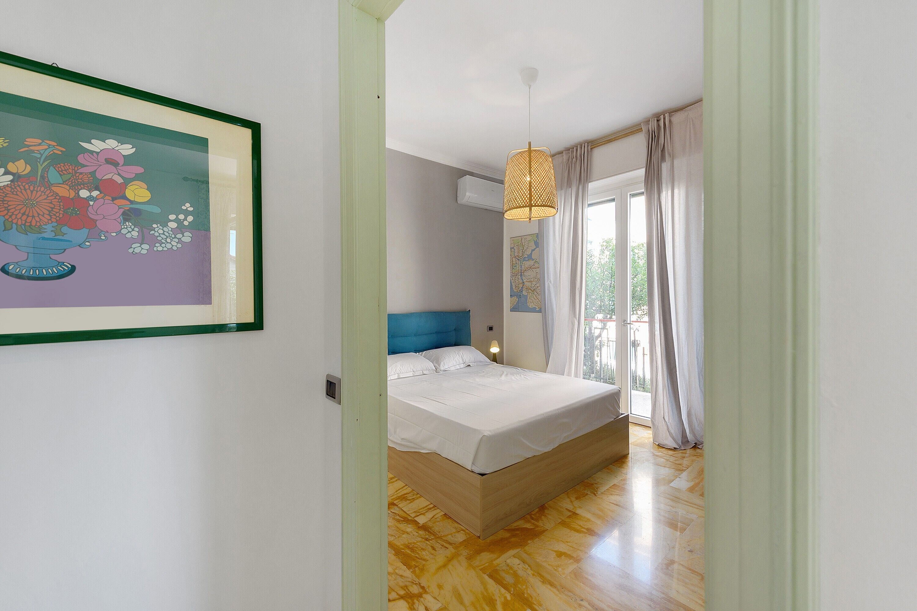 A bedroom with a bed, a hanging light fixture, and a window with curtains.