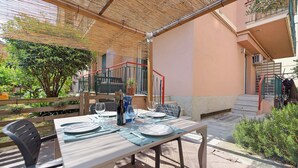 Ein Essbereich im Freien mit einem Tisch für vier Personen, umgeben von Stühlen, einer Pergola und einer Treppe, die zu einer oberen Ebene führt.
