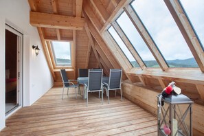Eine Holzterrasse mit Tisch und Stühlen, einer Laterne und Blick durch Dachfenster.