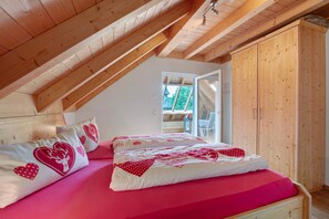 Ein Schlafzimmer mit schrägen Wänden, einem Holzschrank und einem Bett mit Bettwäsche mit Herzmuster.