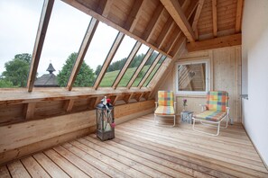 Eine Holzterrasse mit geneigter Decke, zwei Stühlen, einem Laternen und einem Fenster.
