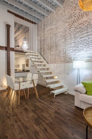 Un interior moderno con una escalera, un comedor con mesa de vidrio y un sofá blanco.