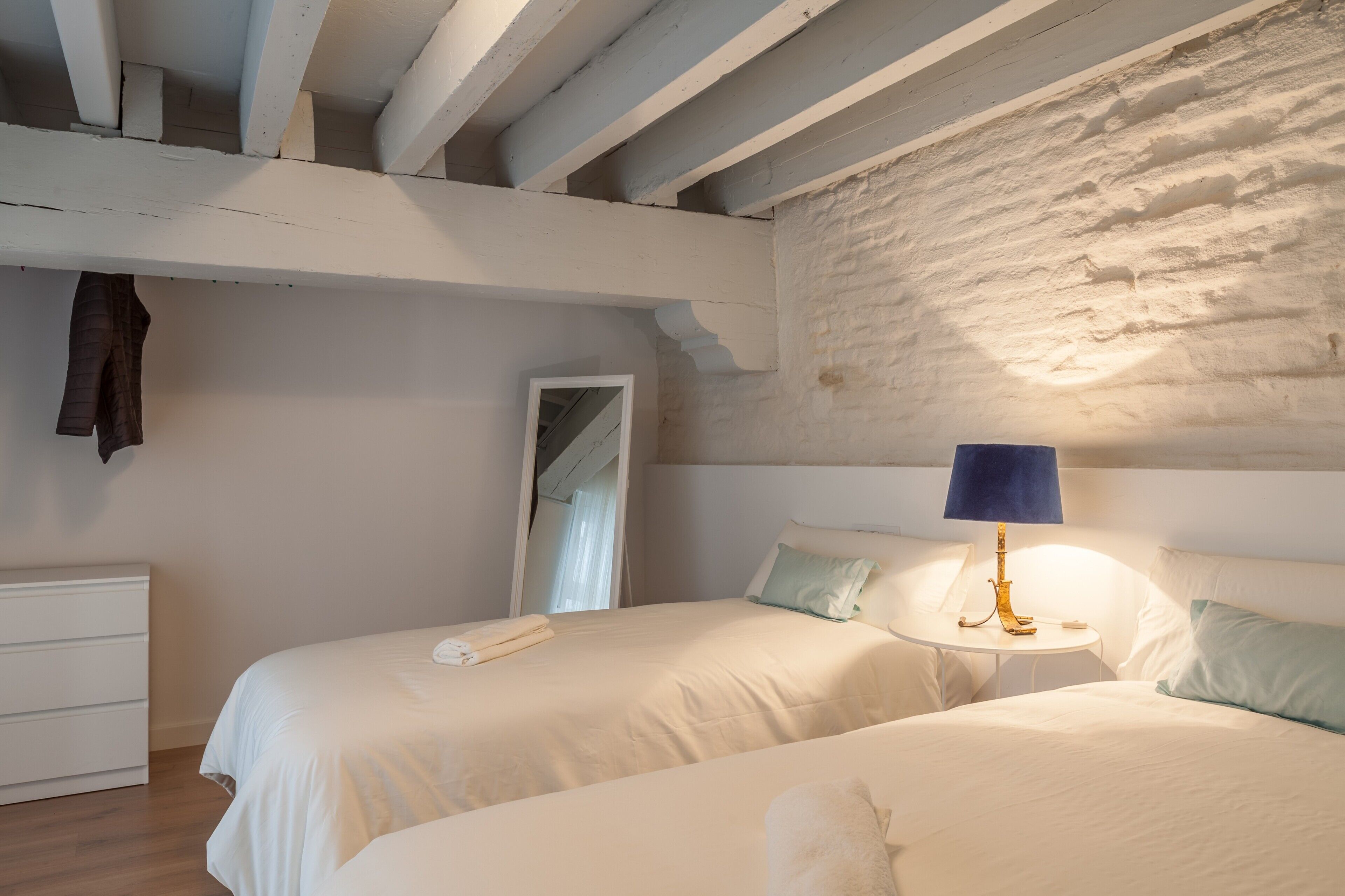 Ein Schlafzimmer mit zwei Betten, einem kleinen Tisch mit Lampe, einem Schminktisch und einem Spiegel.