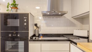 Een keuken met een ingebouwde oven, een roestvrijstalen afzuigkap en een witte betegelde spatwand.