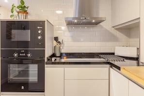 Una cocina con horno empotrado, extractor de acero inoxidable y salpicadero blanco de azulejos.