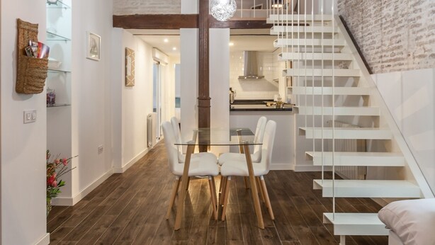 Een modern interieur met een houten eettafel, witte stoelen, een hanglamp en een witte trap.