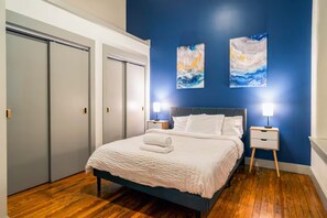 Een slaapkamer met een bed, twee nachtkastjes en twee abstracte schilderijen aan de muur.