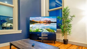 En moderne stue med et fladskærms-tv på et stativ, et træbord og en potteplante.