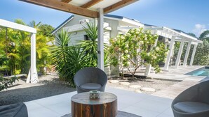 Eine Terrasse im Freien mit einem runden Holztisch, grauen Sitzgelegenheiten mit Polstern und einer weißen Pergola.