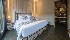 Un dormitorio con una cama grande, mesitas de noche, un espejo y un baño con lavabo y espejo.