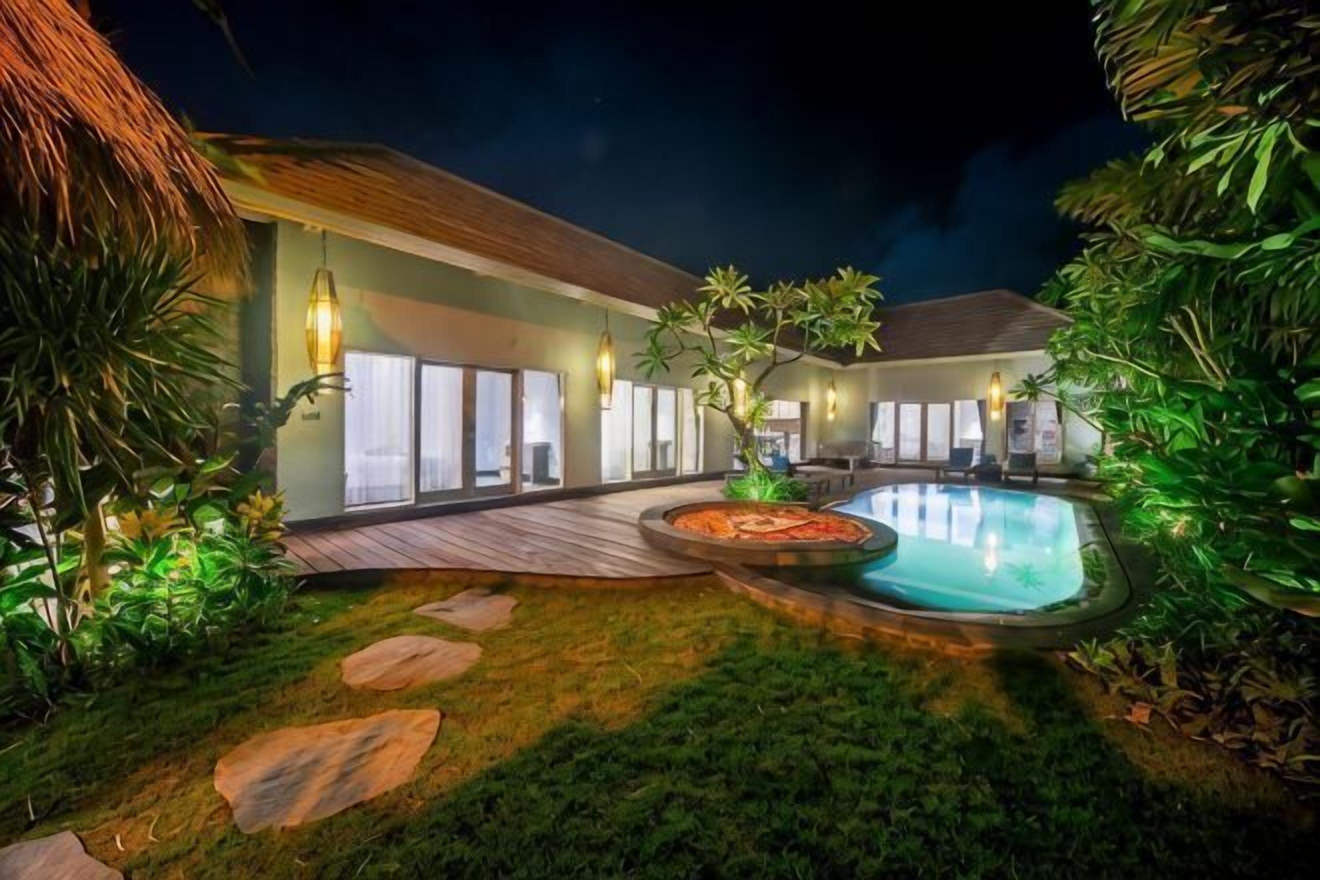 A well-lit outdoor area with a swimming pool, wooden deck, and surrounding greenery.