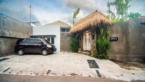 Una casa con tejado de paja, un coche estacionado al frente y un letrero que dice 'SAND VILLA'.