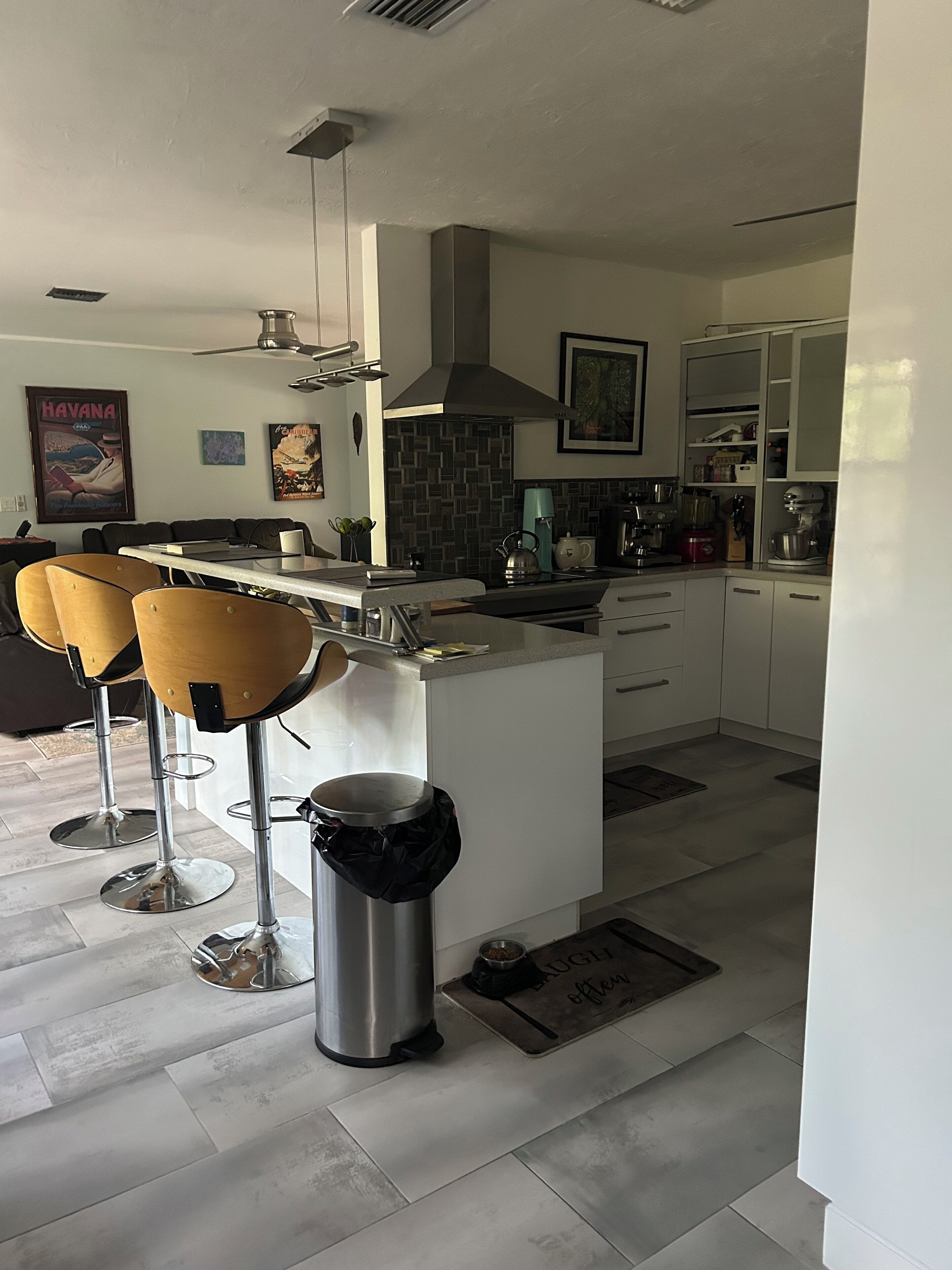 A modern kitchen with a central island, bar stools, a trash can, and a dining area with a table and chairs.