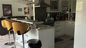 Una cocina moderna con una isla central, taburetes de bar, un bote de basura y una zona de comedor con mesa y sillas.