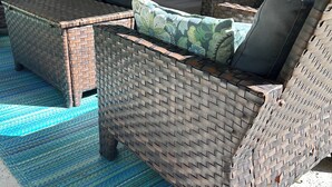 Un conjunto de sofá de mimbre con un tapete azul estampado, un adorno en la pared y una botella de Brew sobre la mesa.