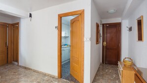 Een gang met een houten deur die leidt naar een keuken, een houten dressoir en een spiegel aan de muur.