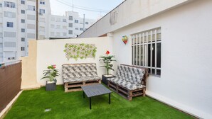 Een klein terras met kunstgras, twee banken, een tafel en potplanten.