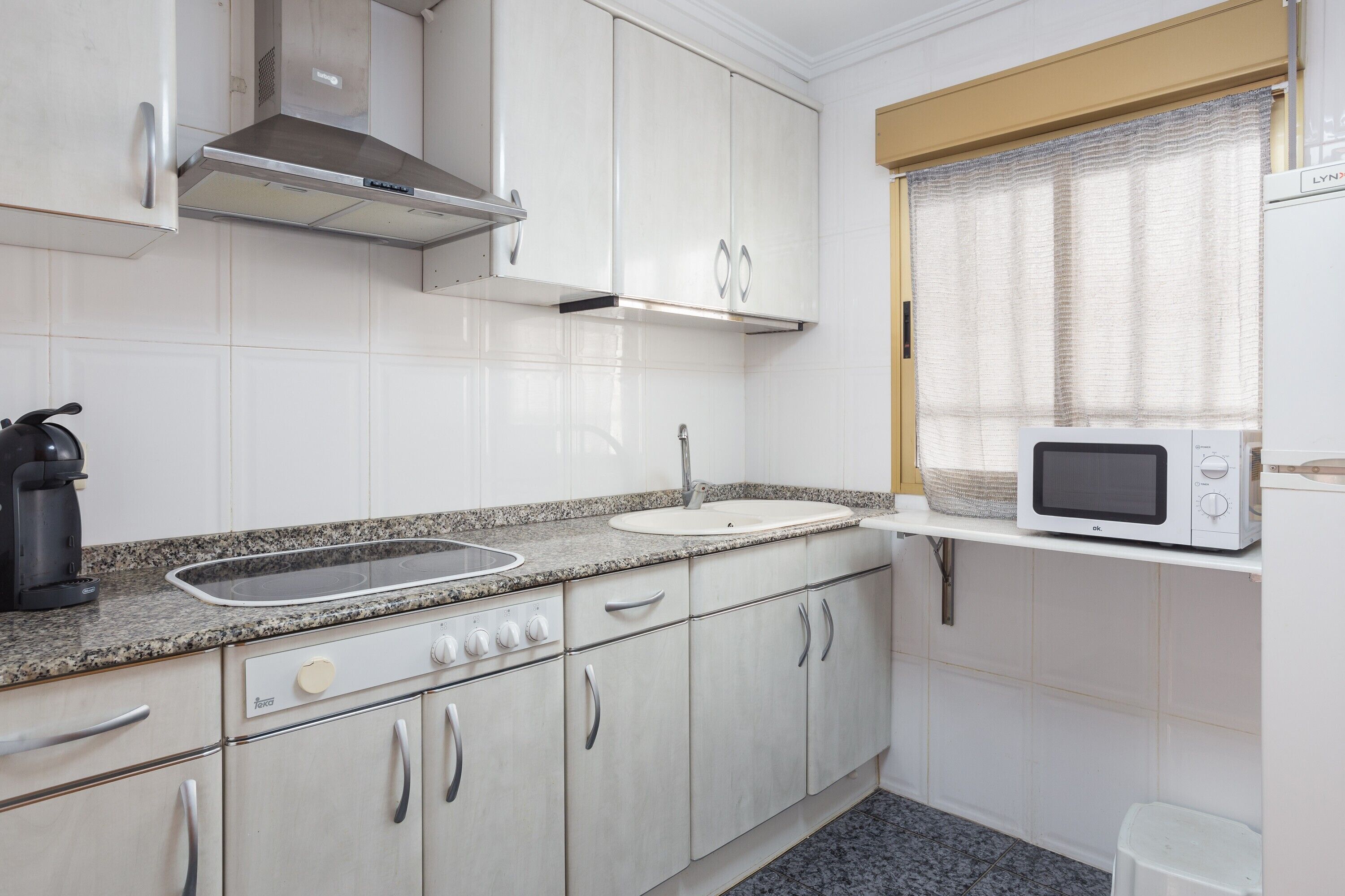 A kitchen with white cabinets, a stainless steel range hood, a microwave, and a sink.