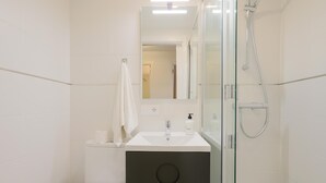 Ein modernes Badezimmer mit Duschkabine aus Glas, einem weißen Waschbecken und einem dunklen Waschtisch.