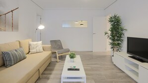 Ein modernes Wohnzimmer mit einer Couch, einem Sessel, einem Couchtisch, einem Fernseher und Topfpflanzen.