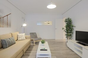 Moderni olohuone, jossa on sohva, nojatuoli, sohvapöytä, televisio ja ruukkukasveja.