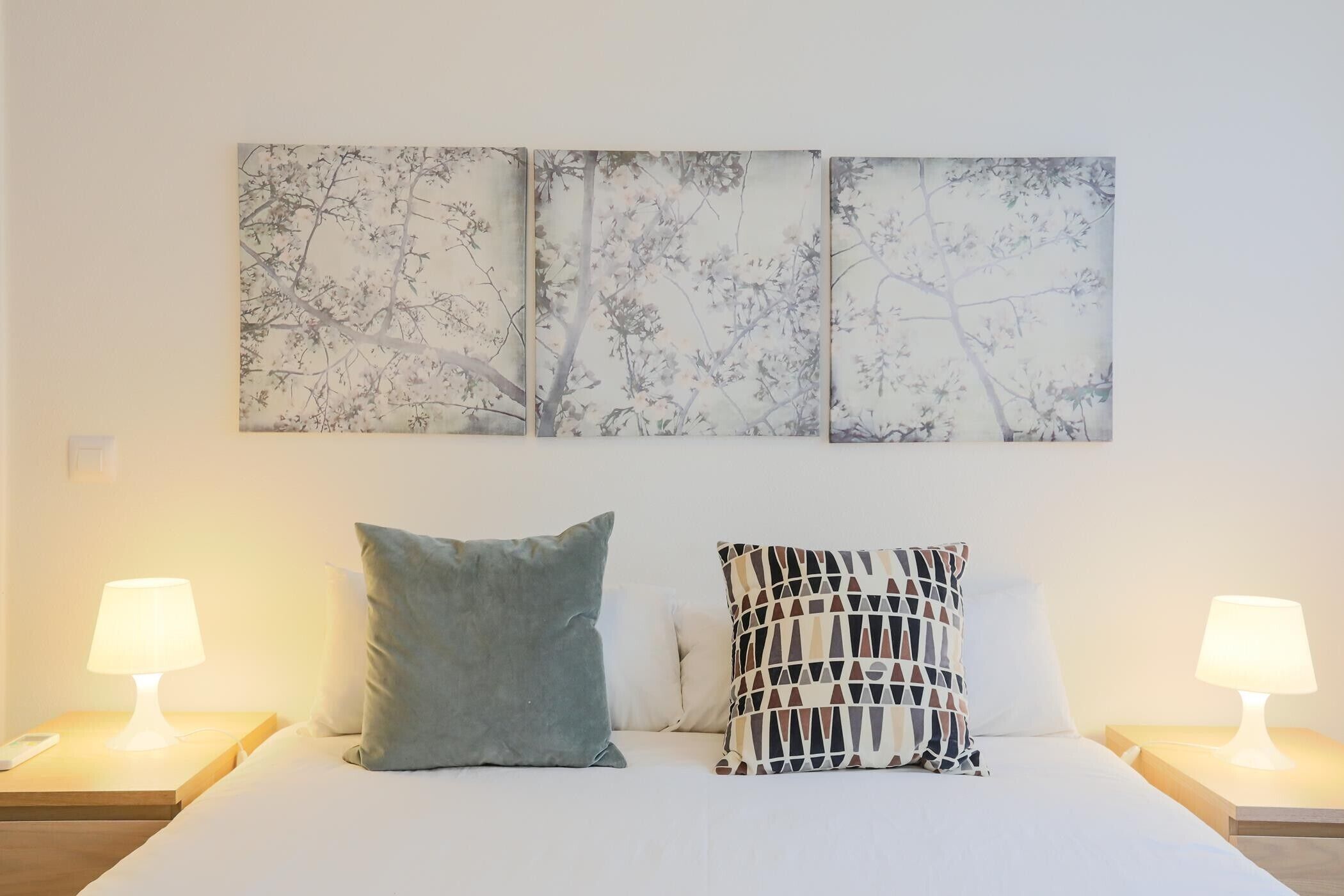 Un letto con due cuscini, un comodino con una lampada e una parete con tre opere d'arte incorniciate.