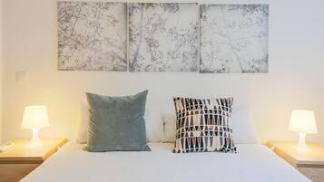Un letto con due cuscini, un comodino con una lampada e una parete con tre opere d'arte incorniciate.
