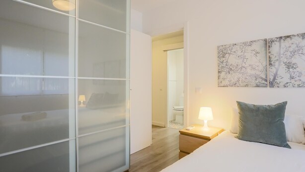 Ein Hotelzimmer mit Bett, Nachttisch mit Lampe, einer Schiebetür und einem Bild an der Wand.