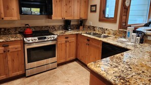 Une cuisine dotée de meubles en bois, d’une cuisinière en acier inoxydable, de plans de travail en granit et d’une fenêtre avec des stores.