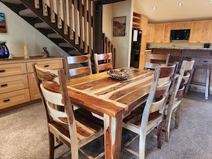 A dining area with a wooden table and chairs, a kitchen with wooden cabinets, and a staircase with wooden railings. - Snowcreek Resort Vacation Rental 224 (Mammoth Lakes)
