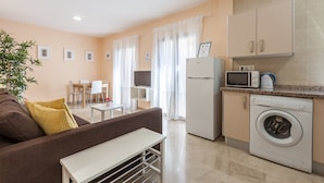 Een modern appartement met een bank, een kleine tafel, een wasmachine, een magnetron en een televisie in de woonkamer.