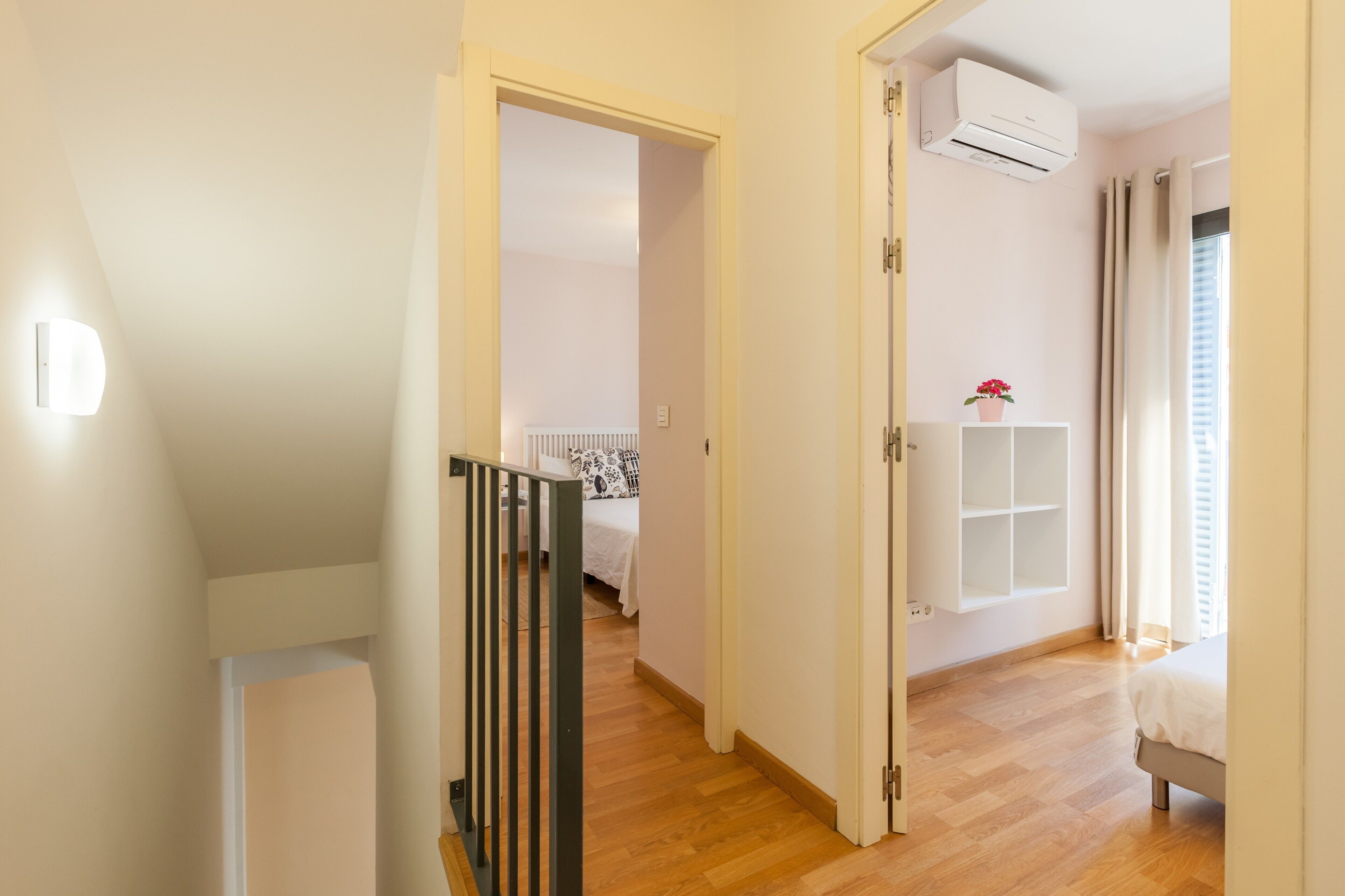 Ein Flur, der zu einem Schlafzimmer mit einem Bett, einem Heizkörper, einer Klimaanlage und einem Fenster mit Vorhängen führt.