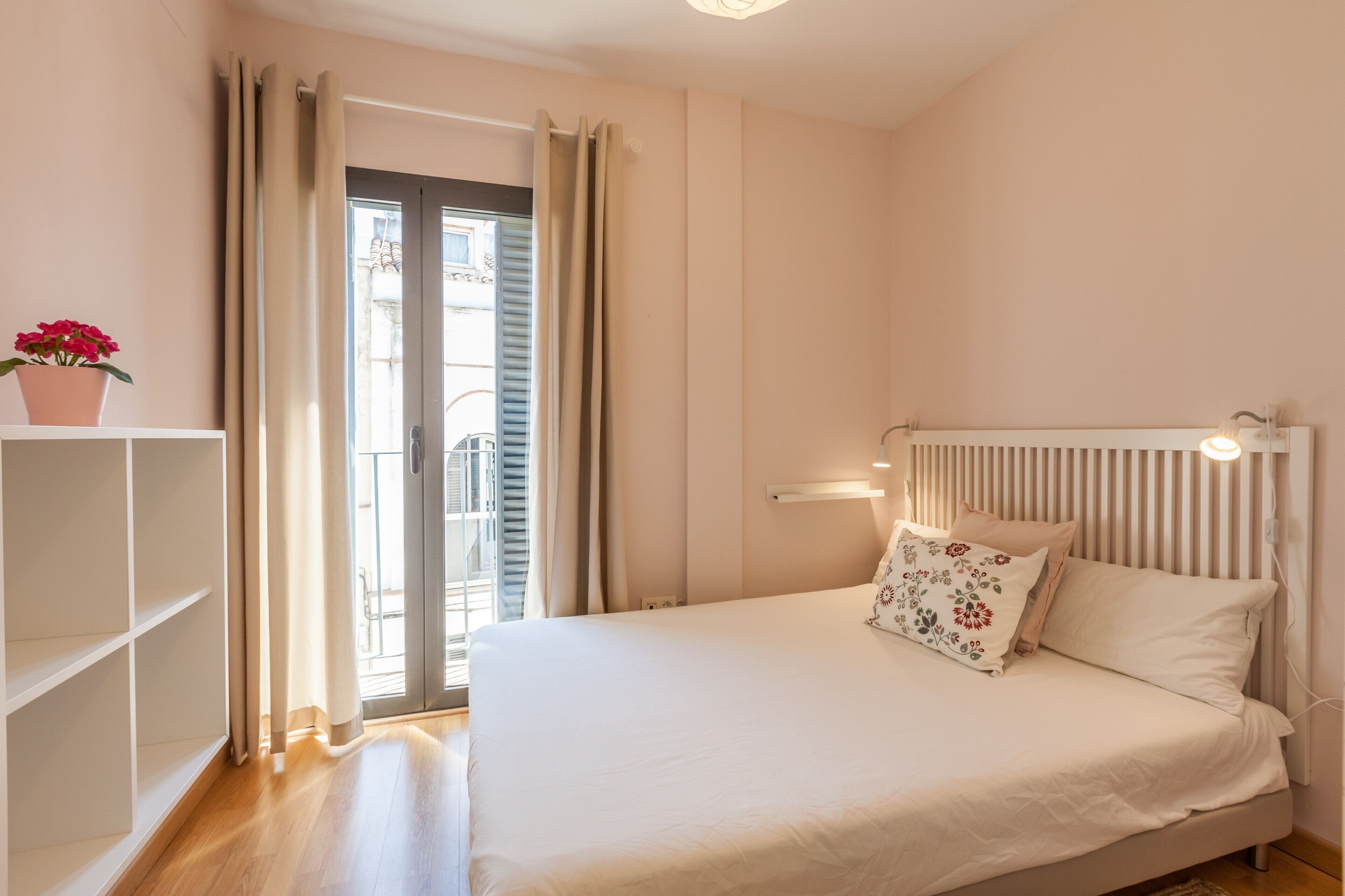 Une chambre à coucher avec un lit, un radiateur, une plante en pot et une vue par la fenêtre, qui est ornée de rideaux.