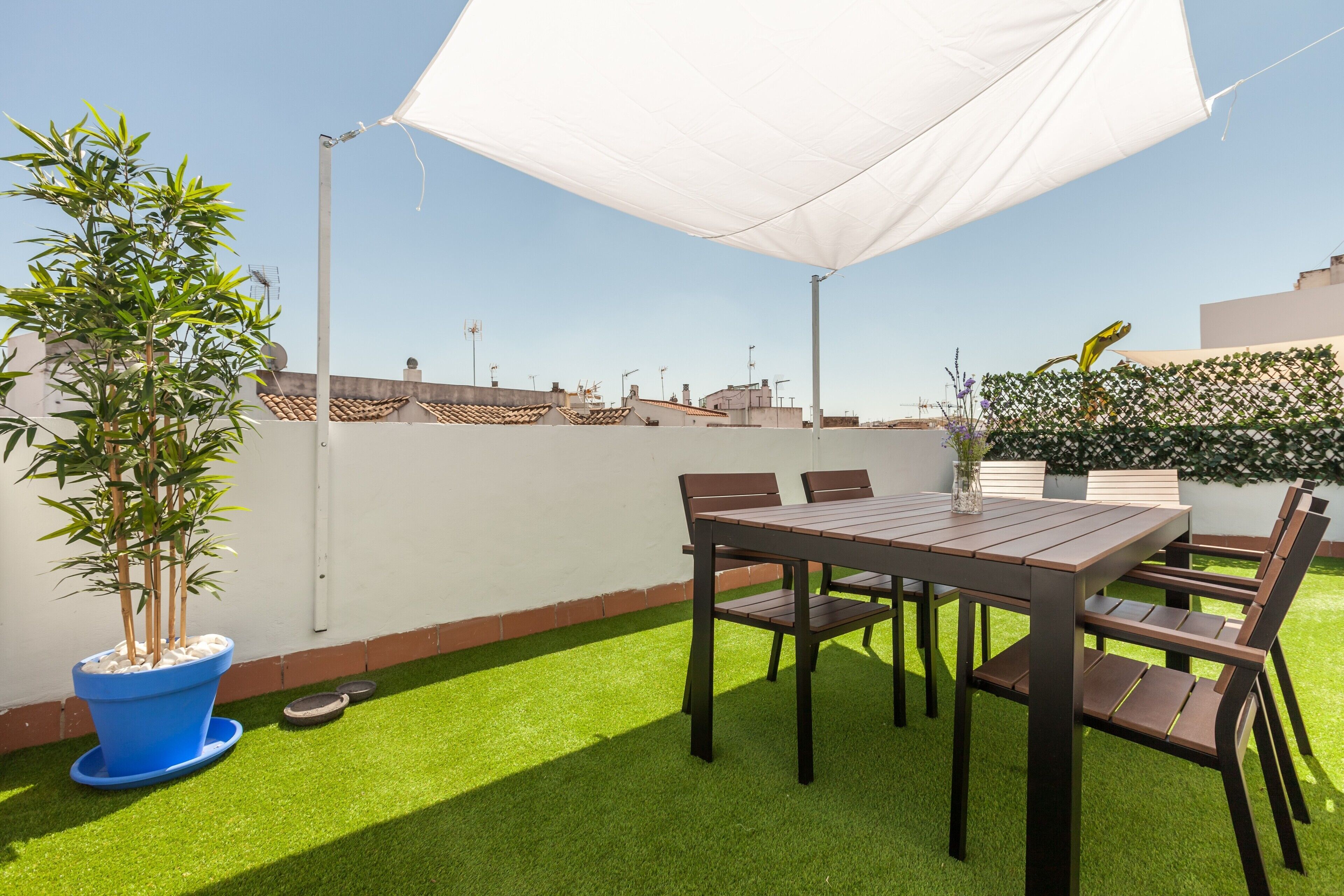 Une terrasse sur le toit avec une table et des chaises, un pot de fleurs et un parasol blanc.