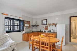 Una cucina compatta con mobili impiallacciati in legno, un tavolo da pranzo con sedie, un frigorifero e una finestra con tende decorative.