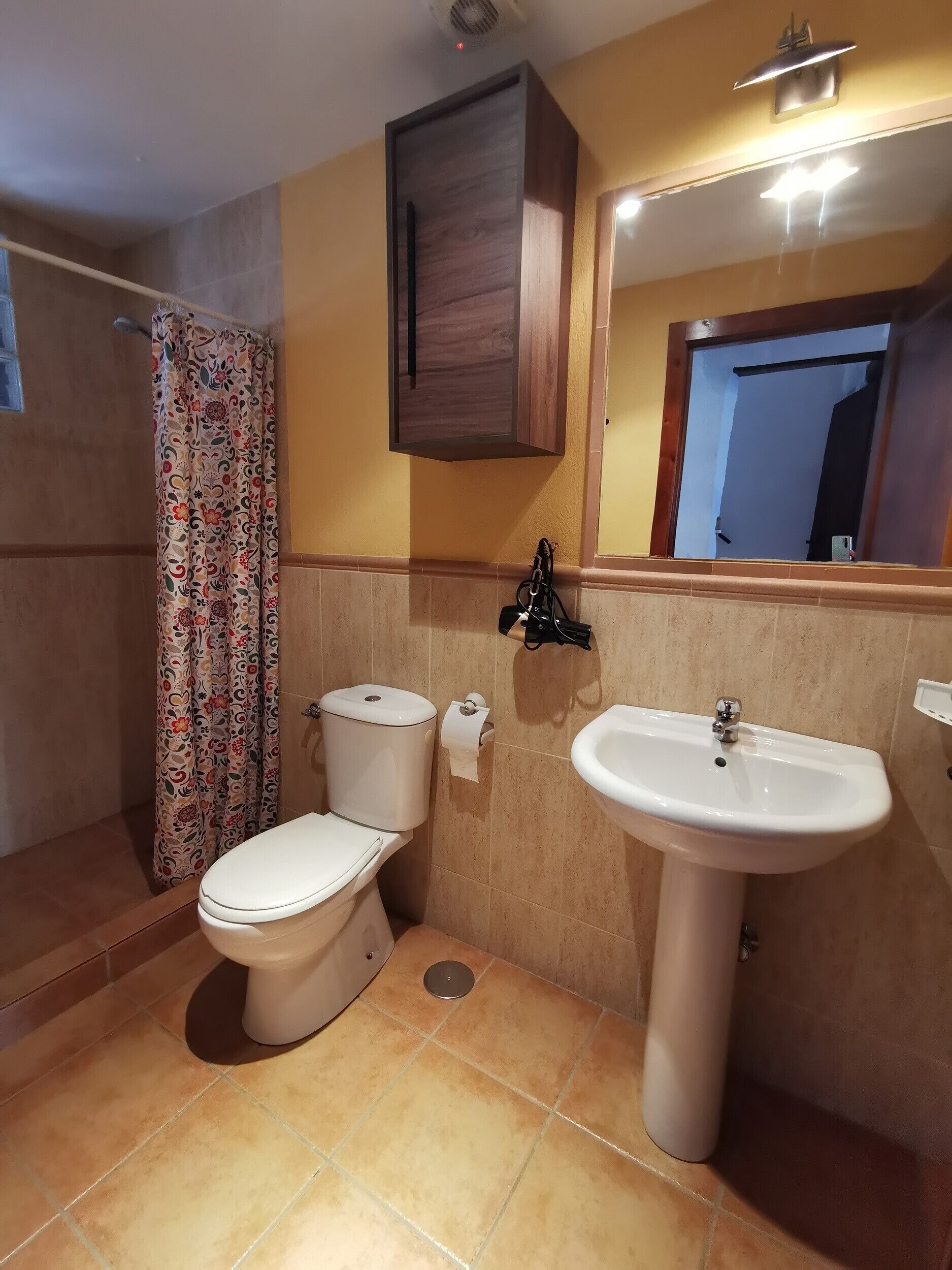 Un baño con inodoro, bidé y lavamanos, cortina de ducha y espejo sobre el lavamanos.