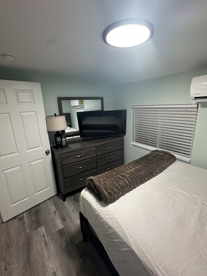 Un dormitorio con cama, cómoda, televisor y luz en el techo.