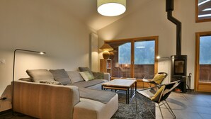 A modern living room with a sectional sofa, a coffee table, a fireplace, and a large window offering a view of the outdoors. - Les Primeveres - Type Loft 10p (Saint-Jean-de-Sixt)