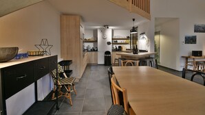 A modern kitchen with wooden cabinets, a dining table, and a staircase. - Les Primeveres - Type Loft 10p (Saint-Jean-de-Sixt)
